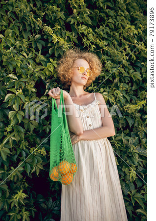 Picture of a young woman in a white dress with a mesh bag with fruits in hands Picture of a young woman in a white dress with a mesh bag with fruits in hands 79173896