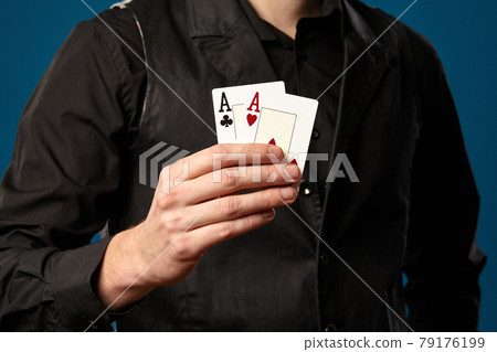Newbie in poker, in black vest and shirt. Holding two playing cards while posing against blue studio background. Gambling, casino. Close-up. 79176199