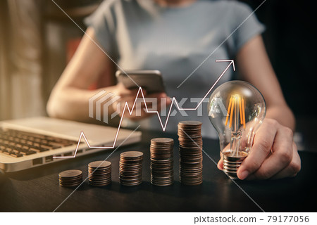Business women hand holding lightbulb and smartphone with coins stack on desk. concept saving energy and money at office. Business women hand holding lightbulb and smartphone with coins stack on desk. concept saving energy and money at office. 79177056