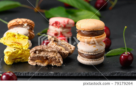 stack of multicolored macarons and ripe red cherries on black wooden background 79179264