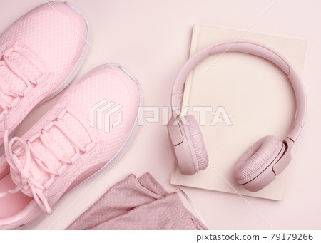 pink wireless headphones, a pair of sneakers and a notepad on a beige background, top view 79179266