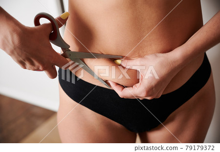 Young woman cutting off excess fat with scissors. 79179372