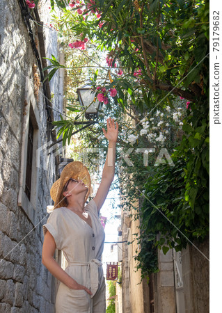 Beautiful blonde young female traveler wearing straw sun hat sightseeing and enjoying summer vacation in an old traditional costal town at Adriatic cost, Croatia. Beautiful blonde young female traveler wearing straw sun hat sightseeing and enjoying summer vacation in an old traditional costal town at Adriatic cost, Croatia. 79179682