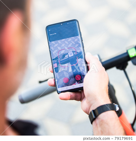 Close up of hand and smartphone, unlocking dockless electric scooter for rent with debranded generic phone app. 79179691