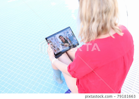 Young woman is holding online business conference via tablet while sitting on edge of pool 79181663