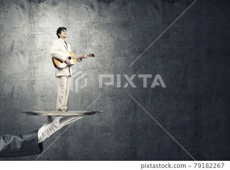 Businessman on metal tray playing acoustic guitar against concrete wall background Businessman on metal tray playing acoustic guitar against concrete wall background 79182267