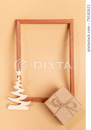 Festive minimal layout with empty wooden frame, small wooden carved decoration - Xmas tree, cardboard gift box on beige background. Christmas or New Year mock up. Top view. Copy space. Vertical photo. Festive minimal layout with empty wooden frame, small wooden carved decoration - Xmas tree, cardboard gift box on beige background. Christmas or New Year mock up. Top view. Copy space. Vertical photo. 79182621