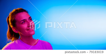Caucasian young woman's portrait on dark studio background in neon. Concept of human emotions, facial expression. Caucasian young woman's portrait on dark studio background in neon. Concept of human emotions, facial expression. 79183019