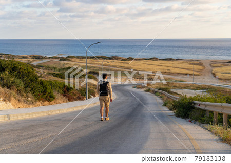 Male tourist hikers on an asphalt mountain road overlooking the sea in Cyprus near Agios Georgios Pegeias. Roadway leading to bay on mediterranean sea. Travel and freedom, adventures and travel Male tourist hikers on an asphalt mountain road overlooking the sea in Cyprus near Agios Georgios Pegeias. Roadway leading to bay on mediterranean sea. Travel and freedom, adventures and travel 79183138