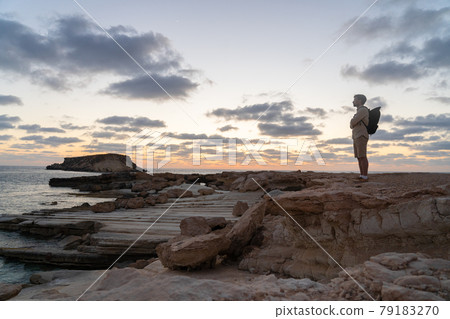Male tourist with backpack watching beautiful view of Yeronisos Holy Island near coast Agios Georgios Pegeias In Cyprus on sunset. Man hiker looks into distance at deserted island in mediterranean sea 79183270