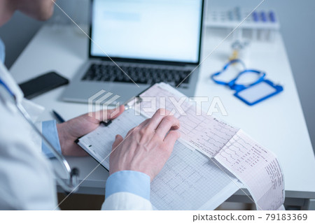 Topic of timely checking for heart disease. Heart disease myocardial infarction. Doctor analyzing electrocardiogram at the desk in hospital office. Cardiologist at work in clinic. doctor look at EKG 79183369