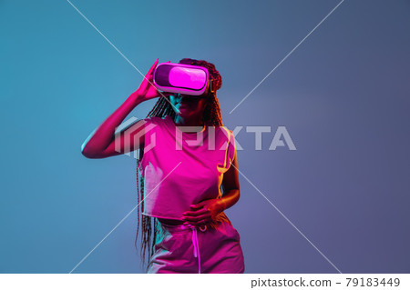 Portrait of young african woman in vr glasses on blue neon background. Concept of virtual reality, entertainment and people. 79183449