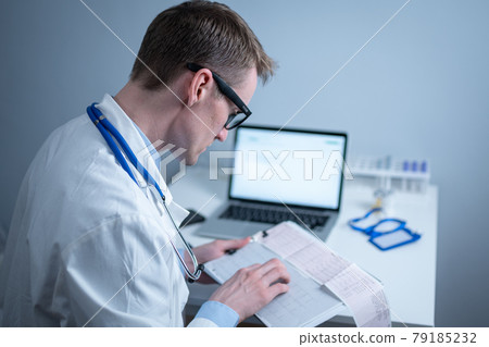 Cardiologist reading an ECG print-out. Doctor analyzing electrocardiogram. Practitioner examine patient test results. Medical and healthcare concept. Physician looking at cardiogram at medical office 79185232