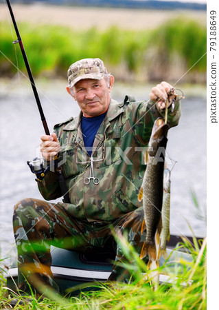 An elderly fisherman in camouflage shows the catch. Opening of the fishing season. An elderly fisherman in camouflage shows the catch. Opening of the fishing season. 79188649