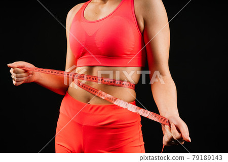 Fitness woman with tape measure showing her waist on studio background 79189143