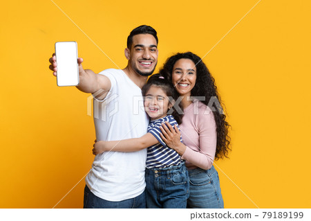 Cheerful Arab Family Of Three Demonstrating Blank Smartphone With White Screen 79189199