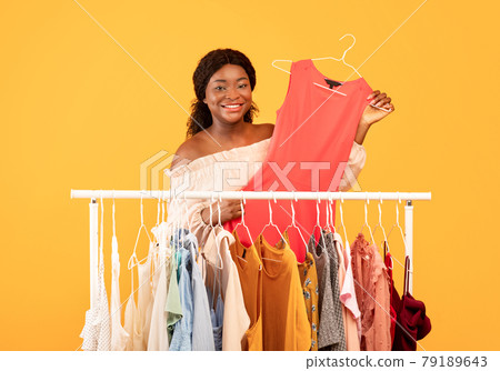 Shopping and summer fashion. Black woman taking hanger with elegant dress from clothing rack, picking new trendy look 79189643