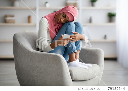 Upset Black Muslim Woman in Hijab Reading Message On Smartphone At Home Upset Black Muslim Woman in Hijab Reading Message On Smartphone At Home 79189644