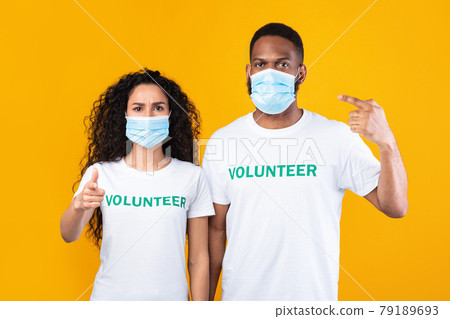 Two Multiracial Volunteers Pointing At Their Face Masks, Yellow Background 79189693