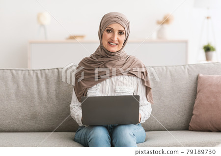 Happy Senior Muslim Lady Using Laptop At Home, Wearing Hijab Happy Senior Muslim Lady Using Laptop At Home, Wearing Hijab 79189730