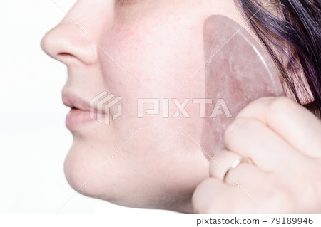 woman massages cheek with quartz scraper close up 79189946