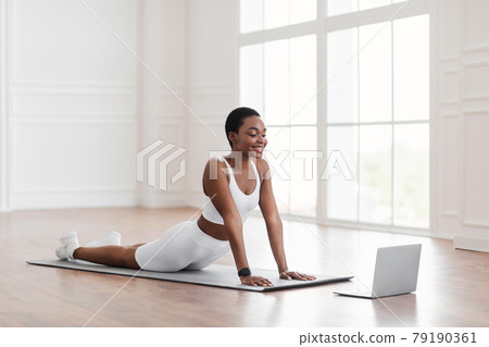 Young african woman stretching back on mat with pc Young african woman stretching back on mat with pc 79190361