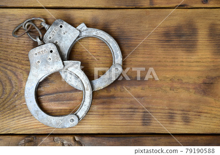 Old and rusty police handcuffs lie on a scratched wooden surface. The concept of an old crime Old and rusty police handcuffs lie on a scratched wooden surface. The concept of an old crime 79190588