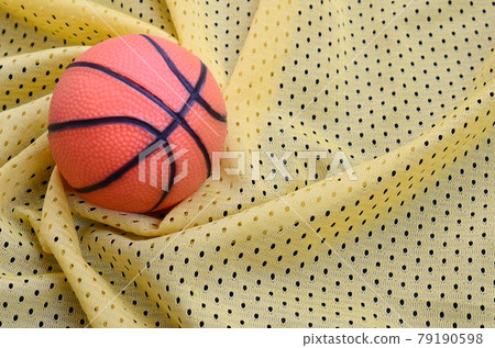 Small orange rubber basketball lies on a yellow sport jersey clothing fabric texture and background with many folds Small orange rubber basketball lies on a yellow sport jersey clothing fabric texture and background with many folds 79190598