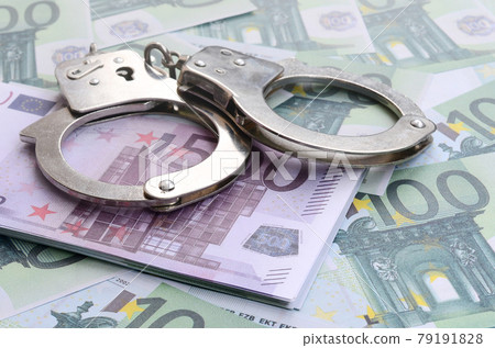 Police handcuffs lies on a set of green monetary denominations of 100 euros. A lot of money forms an infinite heap 79191828