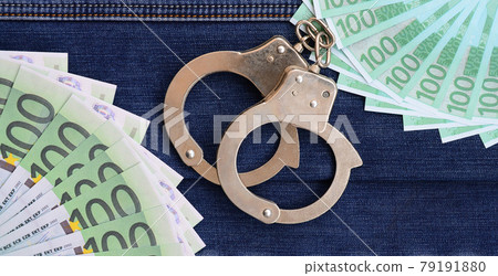 The fan of a lot of euro bills and police handcuffs is on a dark denim surface. Background image 79191880
