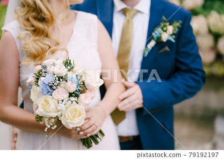 The groom gently touches the bride's hand holding the bouquet during the wedding ceremony The groom gently touches the bride's hand holding the bouquet during the wedding ceremony 79192197