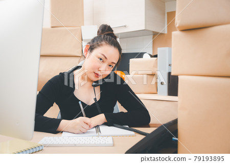 Asian beautiful woman Receiving order by phone and notebooks in selling products online, Working at home the technology to buy and sell of online, preparing products for delivery to customers 79193895
