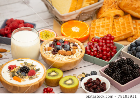 Breakfast Served in the morning with Butter bread and corn flakes Whole grains and raisins with milk in cups and Strawberry, Blueberry, Raspberry, Kiwi, Fresh Orange  on the breakfast table. 79193911