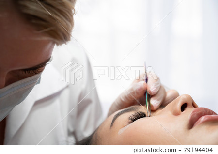 Close-up of a beautiful asian woman on eyelash extension procedure. Double volume false eyelashes. Lashmaker at work. Close-up of a beautiful asian woman on eyelash extension procedure. Double volume false eyelashes. Lashmaker at work. 79194404
