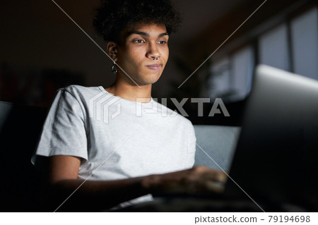 Night portrait of young guy looking at the screen, working on laptop in dark room, sitting on a couch at home Night portrait of young guy looking at the screen, working on laptop in dark room, sitting on a couch at home 79194698