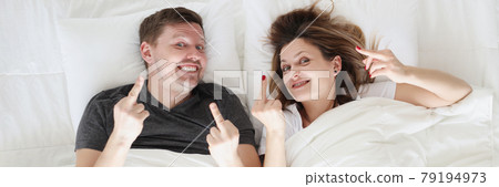 Smiling man and woman lie in bed and call fak gesture 79194973