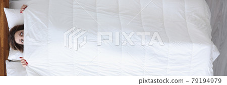 Woman with mad eyes looks out from under covers Woman with mad eyes looks out from under covers 79194979