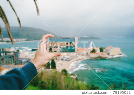 Smartphone with a photo on the screen. In the background is the old town of Budva. Smartphone with a photo on the screen. In the background is the old town of Budva. 79195031