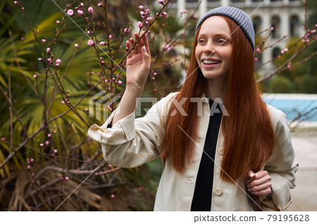 Amazing young red-haired woman in hat posing in Blooming tree at spring, alone Amazing young red-haired woman in hat posing in Blooming tree at spring, alone 79195628