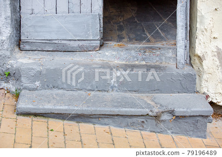 concrete steps entrance to the old house with a wooden door threshold of the building on the descent of the pedestrian sidewalk from stone tiles close-up, nobody. 79196489