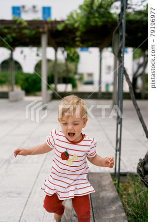 Little girl walks barefoot in the courtyard of the house against the background of a pergola and greenery Little girl walks barefoot in the courtyard of the house against the background of a pergola and greenery 79196977