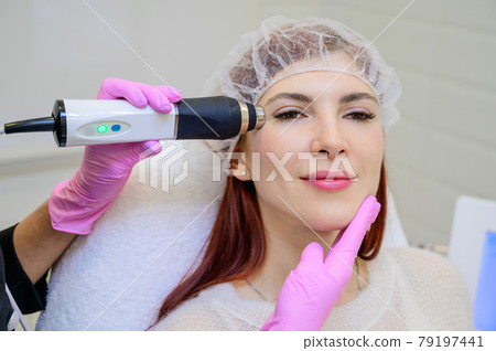 Portrait of a middle-aged woman receiving a non-surgical rejuvenation procedure at a cosmetologist. RF face lifting. Hardware facial massage. Portrait of a middle-aged woman receiving a non-surgical rejuvenation procedure at a cosmetologist. RF face lifting. Hardware facial massage. 79197441