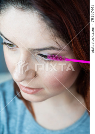 Red head woman brushing her extension eyelashes with a brush. girl with impending eyelid make-up mascara. Beauty industry. Red head woman brushing her extension eyelashes with a brush. girl with impending eyelid make-up mascara. Beauty industry. 79197442