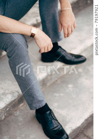 Groom is sitting on the steps in a gray suit and black shoes. Legs close up 79197921