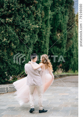 Groom carries bride in his arms along the path in the olive grove on Lake Como, Italy. Back view Groom carries bride in his arms along the path in the olive grove on Lake Como, Italy. Back view 79198080