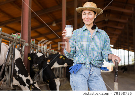 Portrait of a positive kazakh farmer woman in a cowshed, holding a glass of milk 79198756