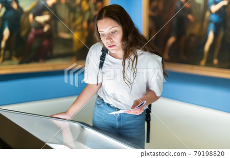 Attentive girl visitor at the museum looks at the exposition behind a glass display case Attentive girl visitor at the museum looks at the exposition behind a glass display case 79198820
