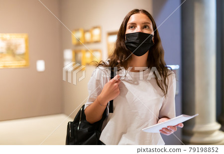 Young girl in a protective mask visits an exhibition of paintings in a museum 79198852