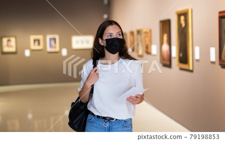 Young girl in a protective mask visits an exhibition of paintings in a museum 79198853