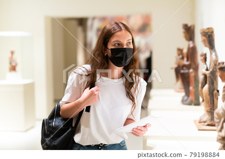 Young girl wearing a protective mask in the museum looks at the exhibits 79198884